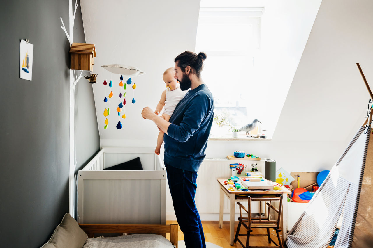 Father holding baby standing in childs bedroom