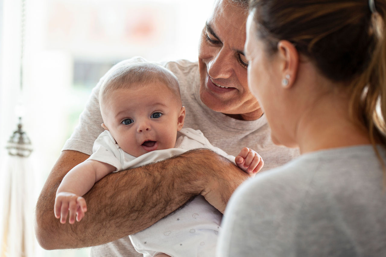 Mother playing with her baby boy while his father holding him on his arms.