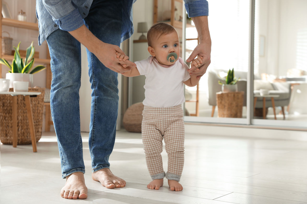 Kleinkind hält sich an Händen von Vater um Gehversuche zu machen