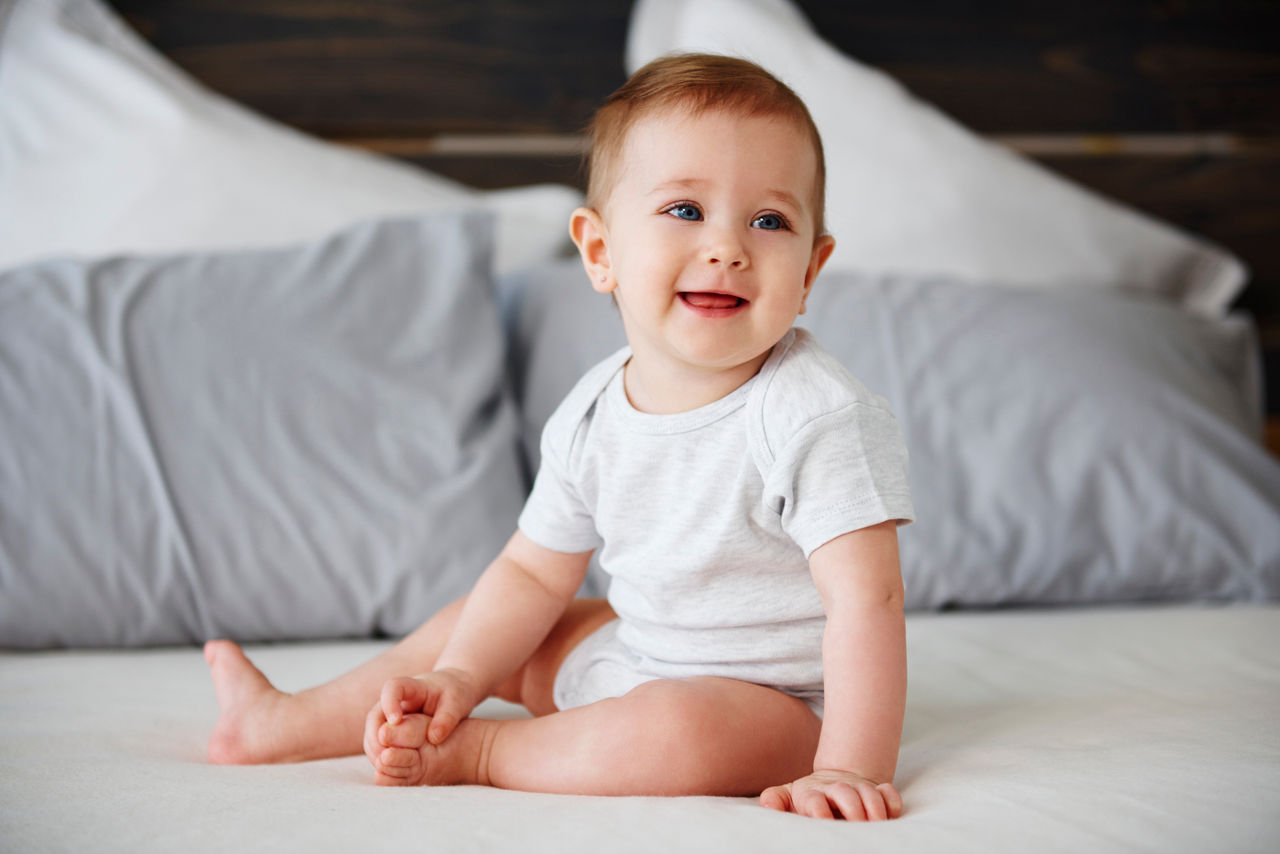Baby on bed sitting and laughing